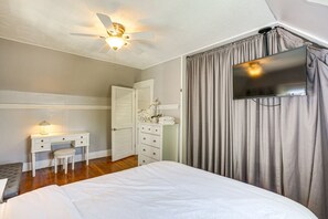 Une chambre à coucher comprenant un lit, un bureau avec une lampe, une armoire, un ventilateur de plafond et un téléviseur fixé au mur.