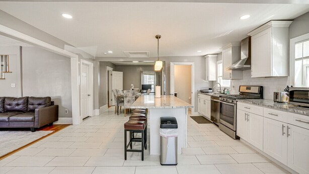 A modern kitchen with white cabinets, a central island, and a dining area with a sofa and chairs.