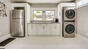 A modern kitchen with white cabinets, a stainless steel refrigerator, and a built-in washer and dryer.