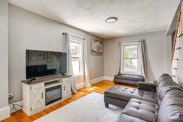 Un salon avec un téléviseur à écran plat posé sur un meuble en bois, un canapé gris et un meuble blanc dans lequel se trouve une cheminée.