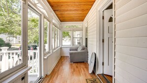 A covered porch with a wooden ceiling, white siding, and a gray sofa.