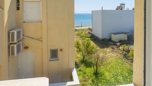 Une vue depuis une fenêtre donnant sur un immeuble surmonté d’un réservoir d’eau, avec un petit jardin et un ciel bleu dégagé.