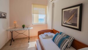 Une petite pièce bien éclairée, avec un lit, une table sur laquelle se trouve une lampe, une fenêtre donnant sur un beau paysage et un tableau encadré accroché au mur.