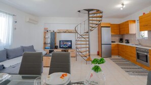 Un appartement moderne doté d’un escalier en colimaçon, d’une cuisine avec des meubles en bois, d’un coin repas avec une table dressée pour deux personnes et d’un salon avec un canapé et des fauteuils.