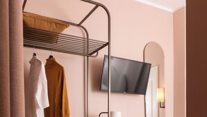 Une salle de bain avec un meuble-lavabo en bois, une chaise ronde, un porte-serviettes avec des vêtements, un téléviseur fixé au-dessus du miroir et un comptoir en marbre.