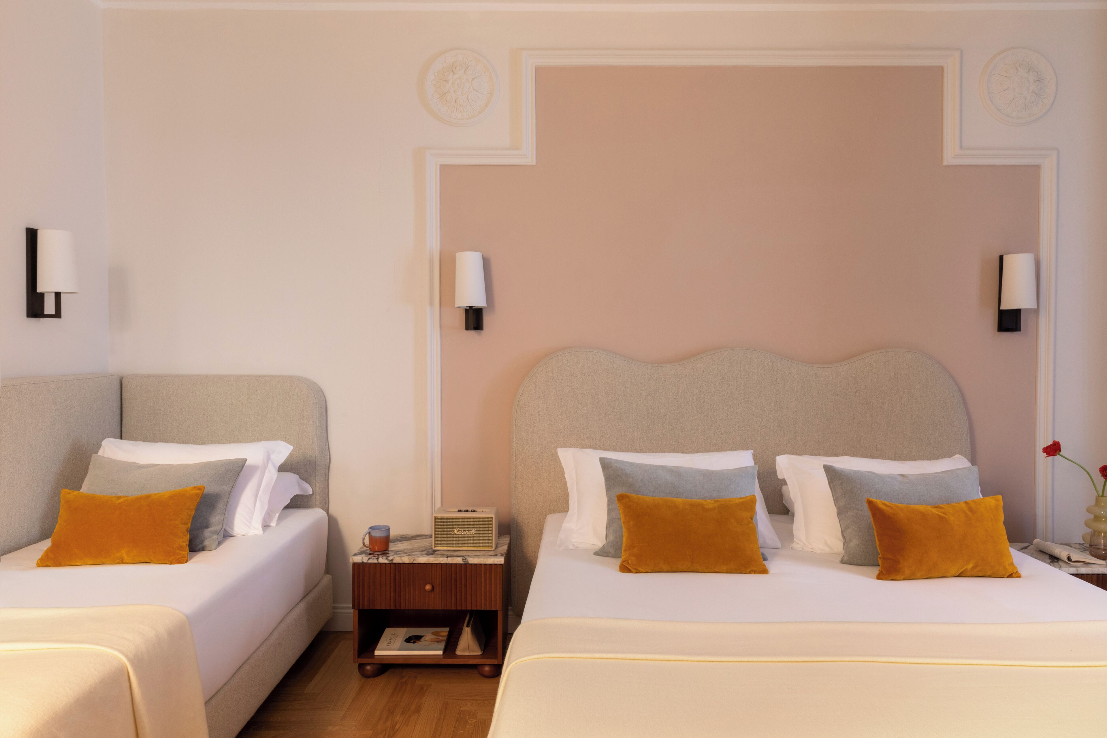 A hotel room with two beds, a nightstand, a radio, and wall-mounted lamps.