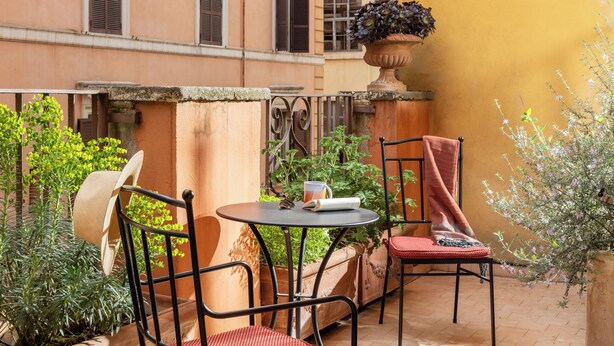 Une cour avec une table et des chaises, un pot de fleurs et la façade d’un immeuble.
