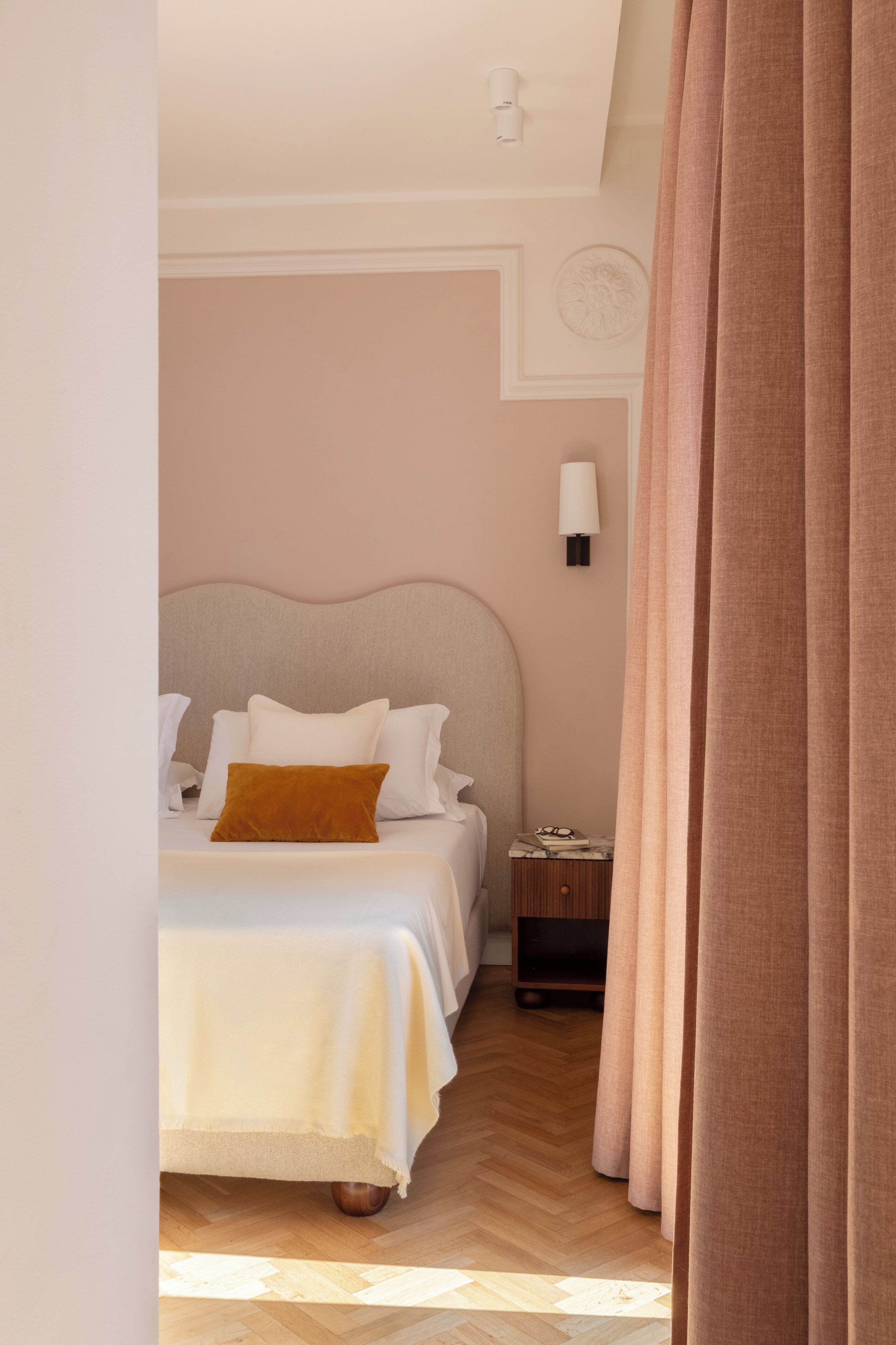 A bedroom with a bed, a nightstand, a lamp, and a curtain.