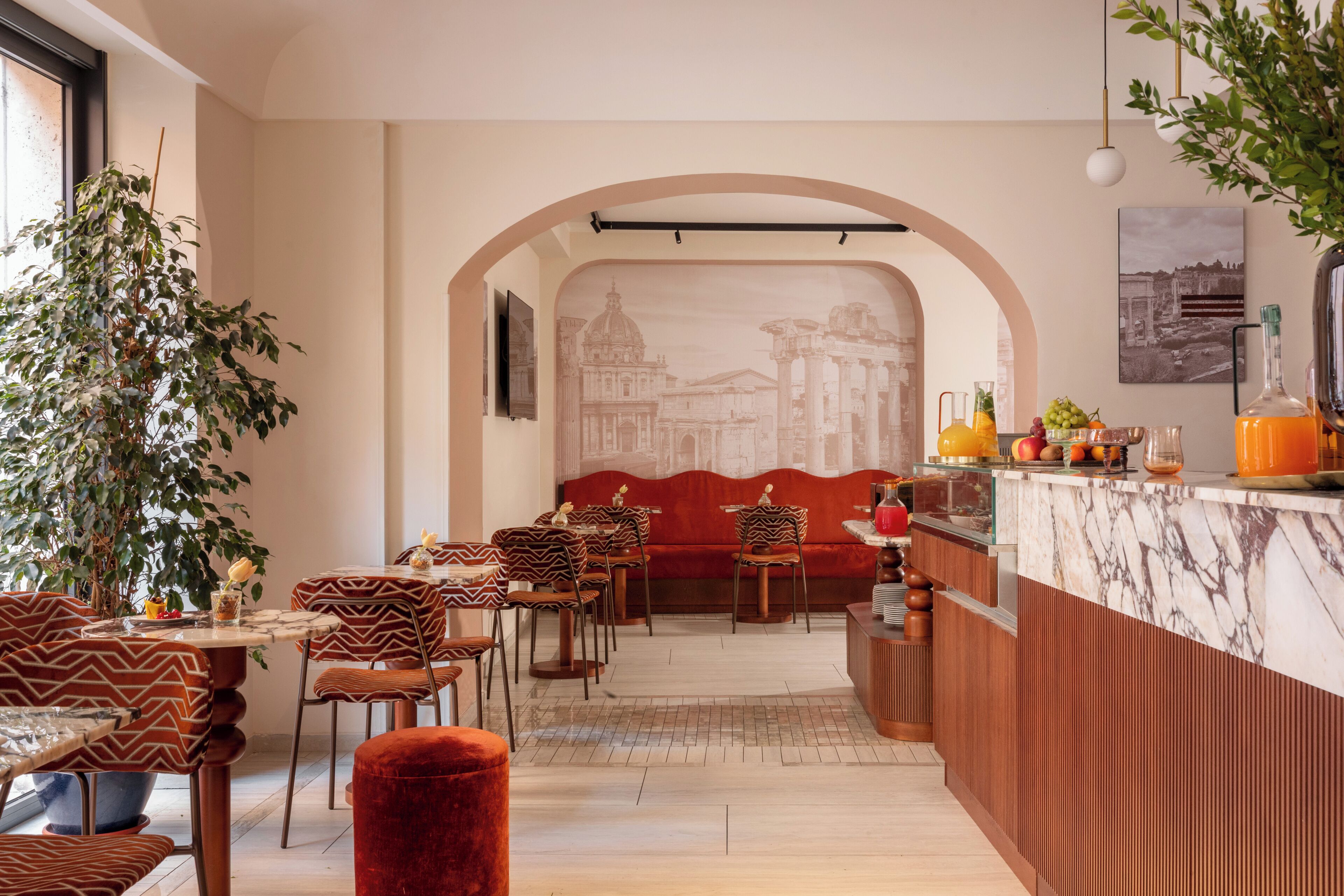A restaurant with a marble counter, red upholstered seating, and a mural of ancient architecture.