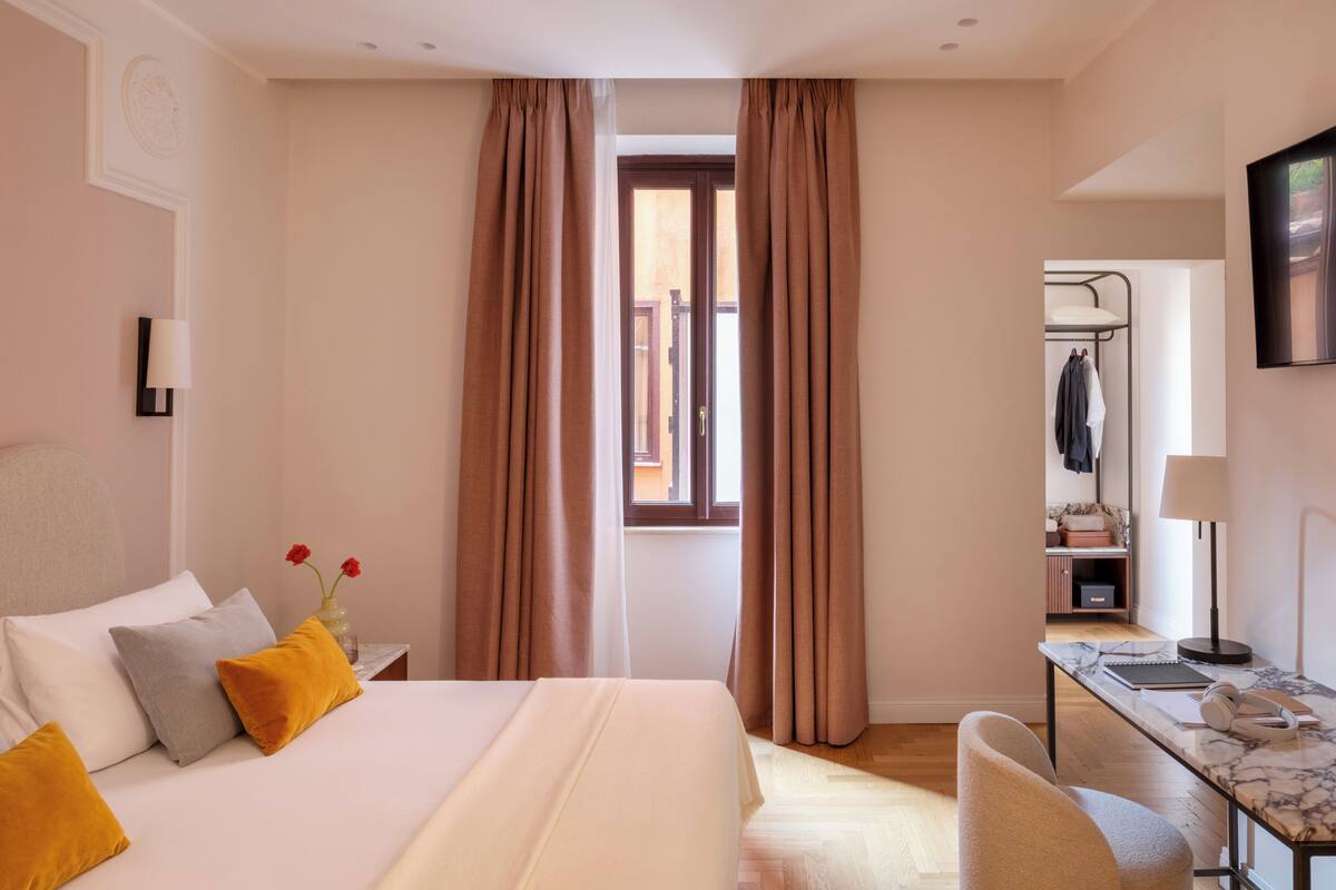 A hotel room with a bed, a desk, a chair, a wardrobe, and a window with curtains.