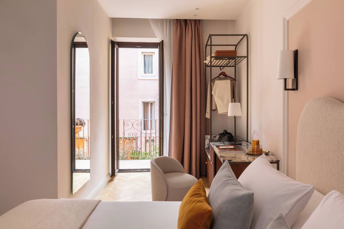 A hotel room with a bed, a desk, a chair, a hanging shelf, and a view of the outside balcony.