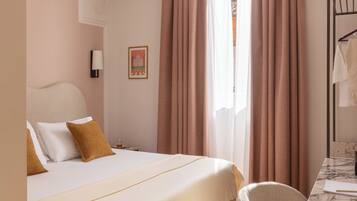 A hotel room with a bed, a chair, a desk, a lamp, and a window with curtains.