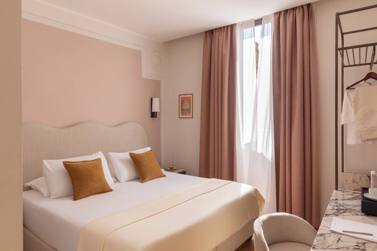 A hotel room with a large bed, a bedside table, a chair, a desk, and a window with curtains.