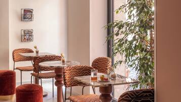 A modern dining area with round tables and patterned chairs, a large window with a view, and a potted plant.