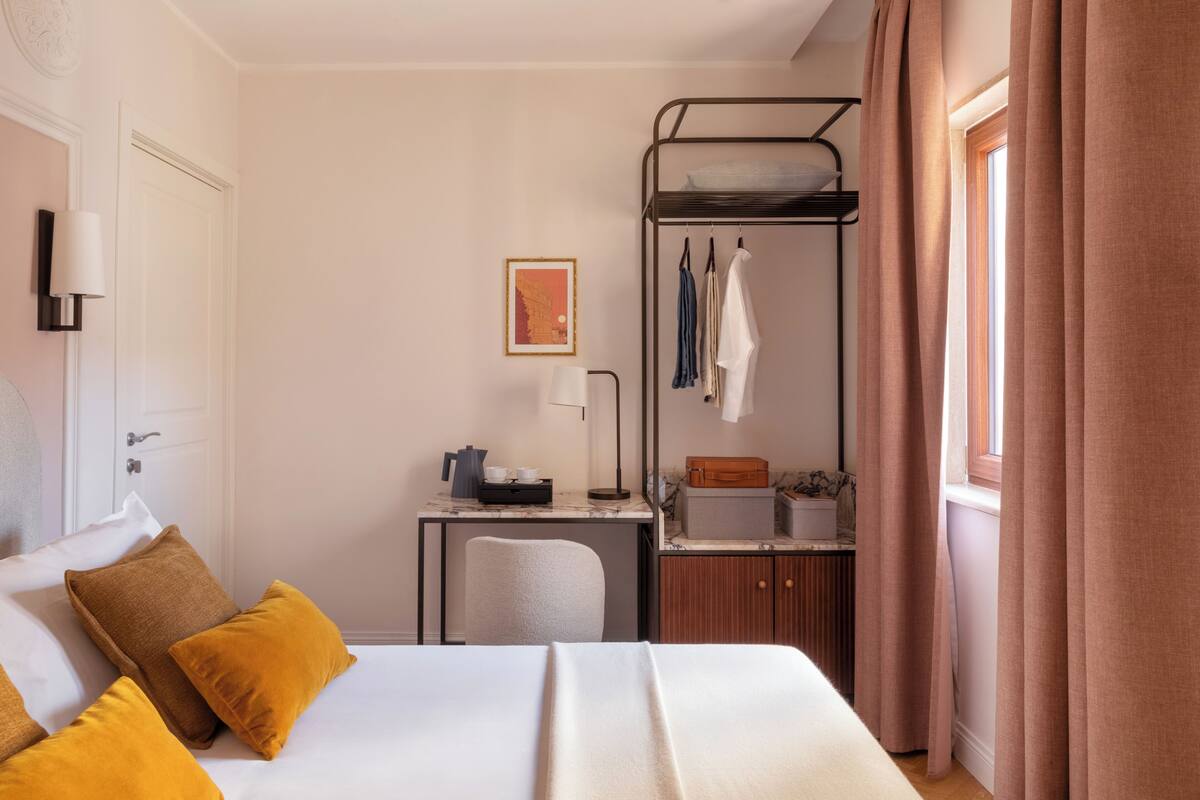 A hotel room with a bed, a desk with a lamp, a bunk bed, and a window with curtains.