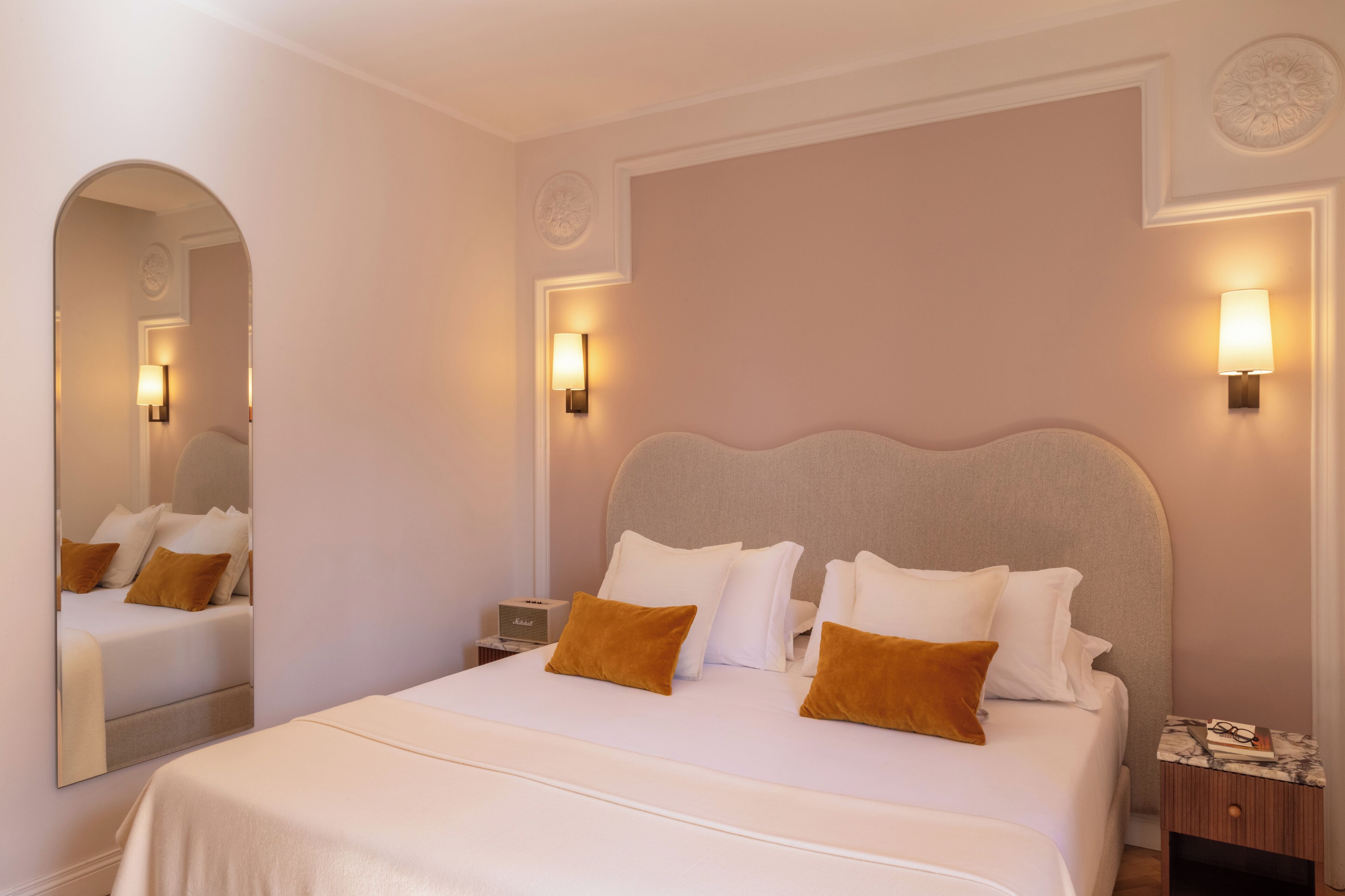 A hotel room with a large bed, two bedside tables, a mirror, and wall-mounted lamps.