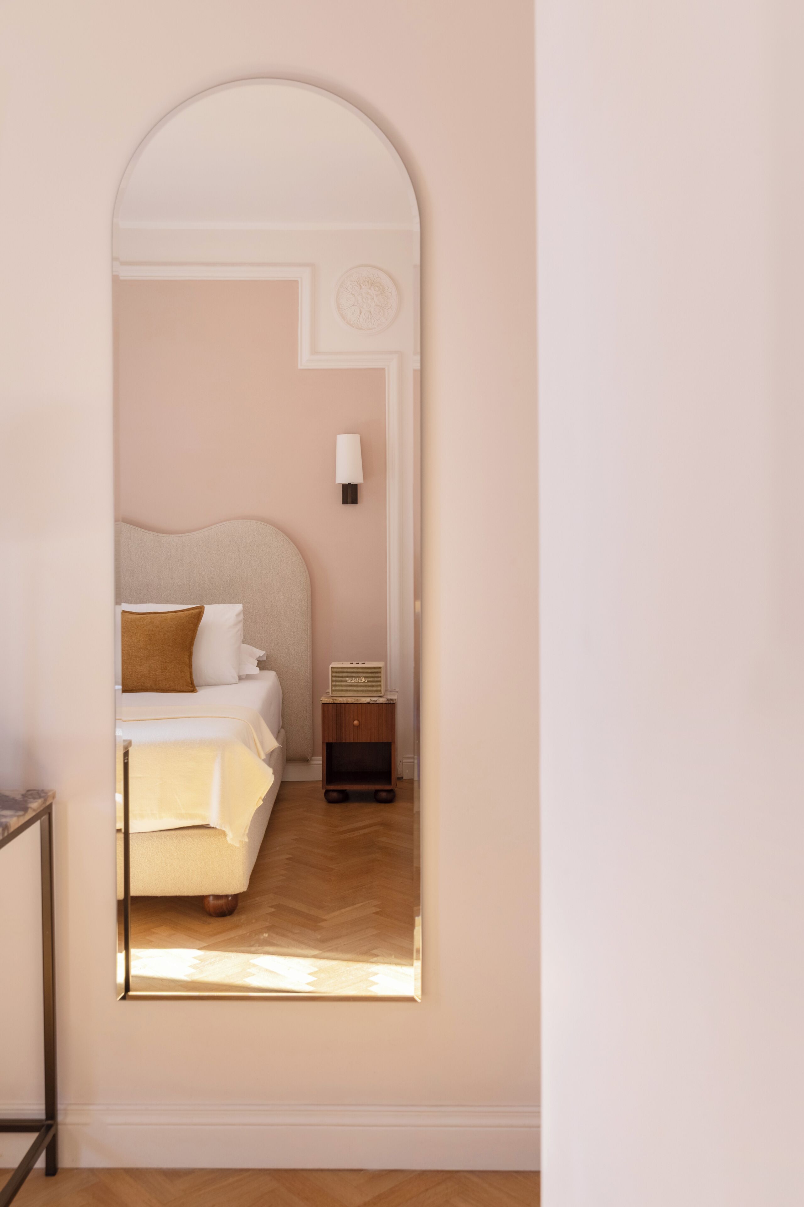 A bedroom with a bed, bedside table, lamp, and a mirror reflecting the room.
