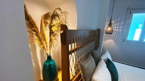 Un dormitorio con cabecera de madera, una mesita de noche con un jarrón de plumas de pampa y una ventana con luz diurna.