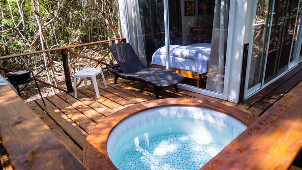 A wooden deck with a hot tub, a lounge chair, and a bed with a glass wall. - La Ballena Nómada (Akumal)