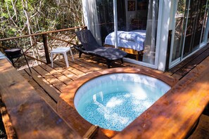 A wooden deck with a hot tub, a lounge chair, and a bed with a glass wall. - La Ballena Nómada (Akumal)