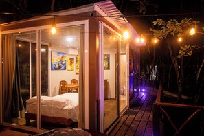 A glass-enclosed bedroom with a bed, a wooden table, and a chair. - La Ballena Nómada (Akumal)