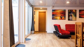 A modern living room with a wooden floor, a red sofa, a black sofa, and a wooden chair. There are three paintings on the wall. - La Ballena Nómada (Akumal)