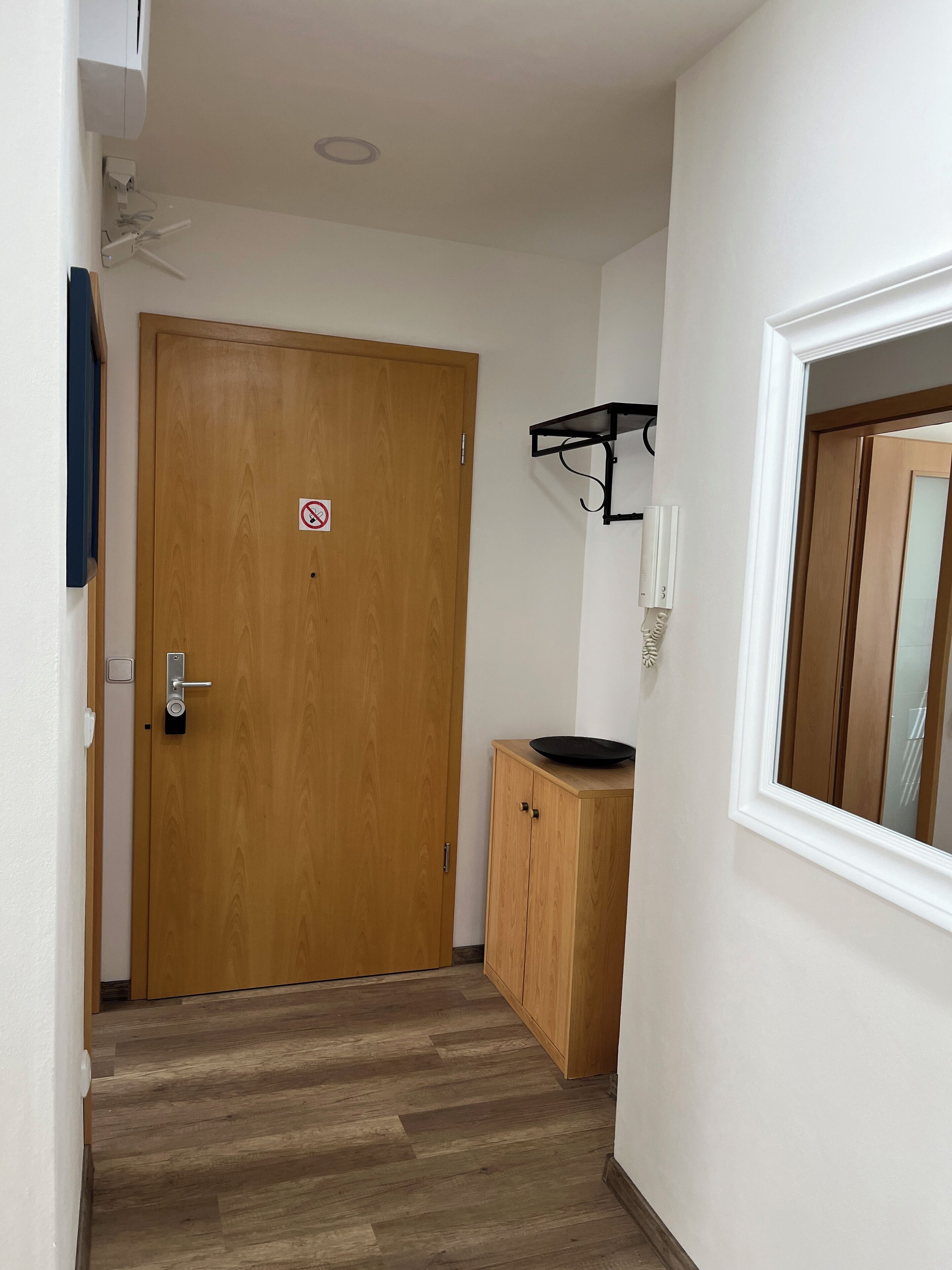 Un couloir avec une porte en bois, une petite armoire et un mur blanc avec une fenêtre.