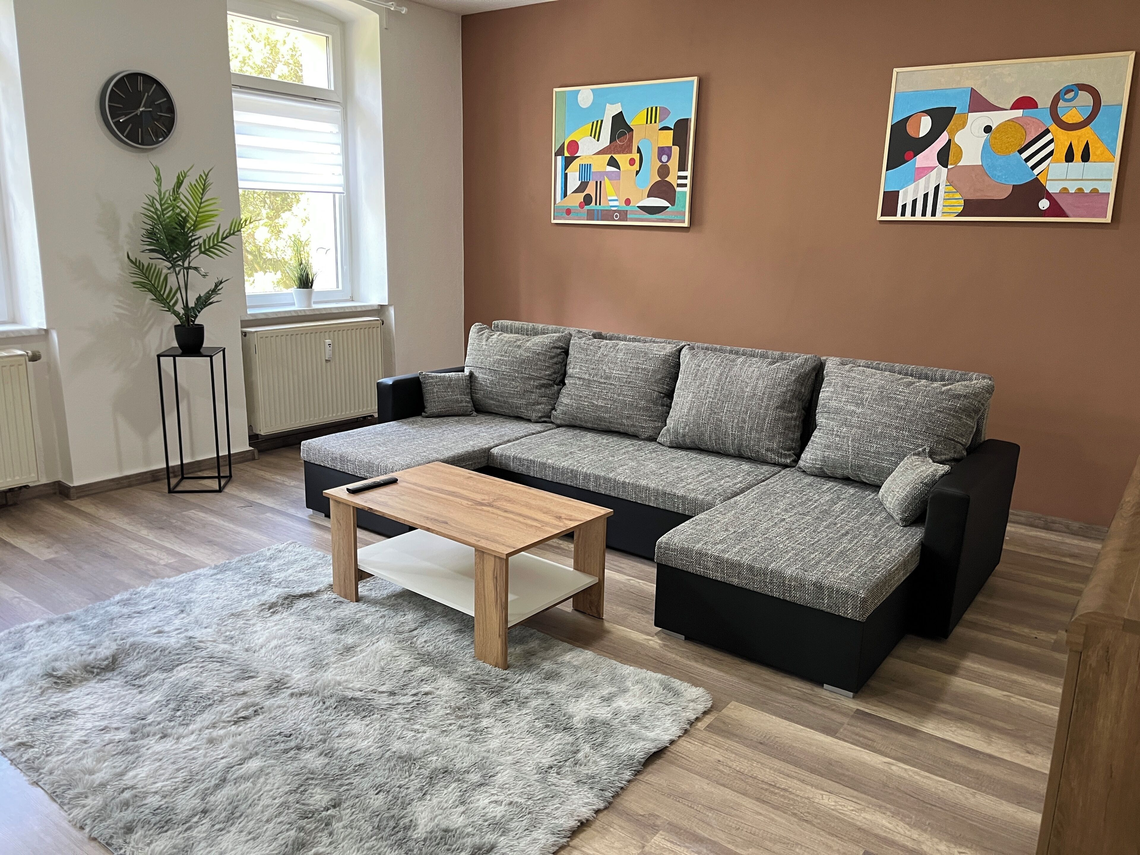 A modern living room with a sectional sofa, a small wooden coffee table, a fluffy rug, a potted plant, and abstract wall art.