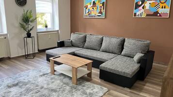 A modern living room with a sectional sofa, a small wooden coffee table, a fluffy rug, a potted plant, and abstract wall art.
