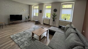 A modern living room with a large sectional sofa, a flat-screen TV, a wooden coffee table, and a grey shag rug.