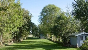A grassy pathway flanked by trees leading to a small building with a shed-like structure. - Ferienhaus Sturmfrei auf Fehmarn (Fehmarn OT Kopendorf)