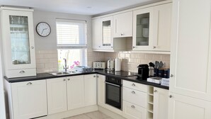 A modern kitchen with white cabinets, a black countertop, a built-in oven, and a window with blinds.