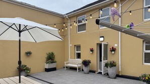 A patio area with a white table and umbrella, potted plants, a white bench, and string lights.