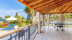 A covered outdoor area with a ping pong table, lounge chairs, and a view of the ocean.