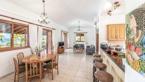 A spacious living area with a dining table, sofas, and a kitchen area with a tiled backsplash and wooden cabinets.