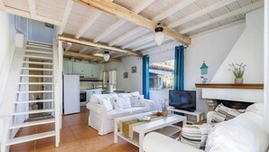 Uma sala espaçosa com um sofá branco, uma mesa de centro, uma televisão e uma escada que dá para uma cozinha.