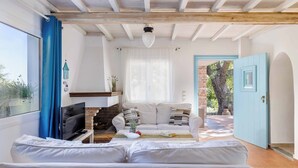 Uma sala de estar acolhedora com um sofá, uma televisão e uma mesa de centro. Há uma lareira e uma porta que dá para o exterior.