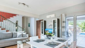 Uma sala de estar moderna com um sofá branco, uma mesa de centro de vidro e uma área de jantar com uma mesa branca posta para quatro pessoas.