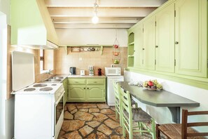 Een keuken met groene kastjes, een witte kookplaat en een vloer met een stenen patroon.