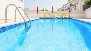 A swimming pool with clear blue water, metal pool ladders, and yellow lounge chairs with red umbrellas. - Villa Ash - Four Bedroom Villa, Sleeps 8 (Alcantarilha)