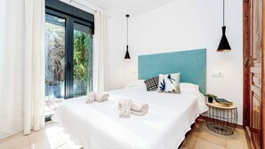 A modern bedroom with a large bed, a view of greenery outside, and a small side table with a book and a plant. - Villa Abeto - Two Bedroom Villa, Sleeps 4 (El Tosalet)