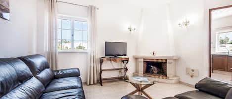 A living room with leather sofas, a television, a fireplace, and a window with curtains.