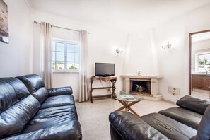 A living room with leather sofas, a television, a fireplace, and a window with curtains. - Villa Arcadia - Eight Bedroom Villa, Sleeps 16 (Vale Rebelho)