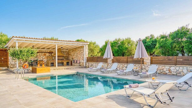 A swimming pool with lounge chairs, a covered seating area, and a stone wall.