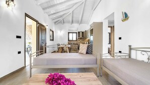 A modern bedroom with a metal bed frame, a wooden table with flowers, and a view of the kitchen and dining area.