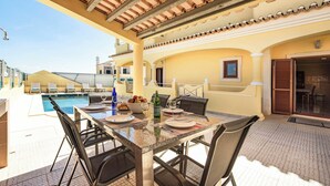 Un espace extérieur abrité, aménagé pour les repas, avec une piscine, des tables, des chaises et une vue sur la piscine.