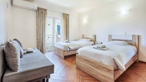 Une chambre d’hôtel avec deux lits en bois, un canapé et une grande fenêtre avec des rideaux.