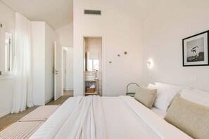Ein Schlafzimmer mit einem großen Bett, ein Badezimmer mit Waschbecken und Spiegel sowie ein gerahmtes Bild an der Wand.