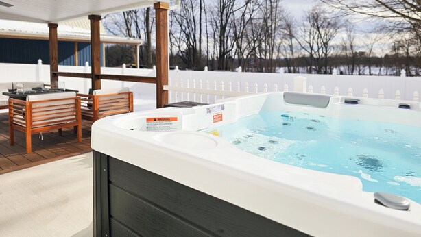 A hot tub with a warning label, a wooden deck, and a white fence in the background. - NEW! Hot Tub, Firepit & Game System Near Hershey - Walk To Lake & Fishing! (Lebanon)