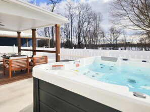 A hot tub with a warning label, a wooden deck, and a white fence in the background.